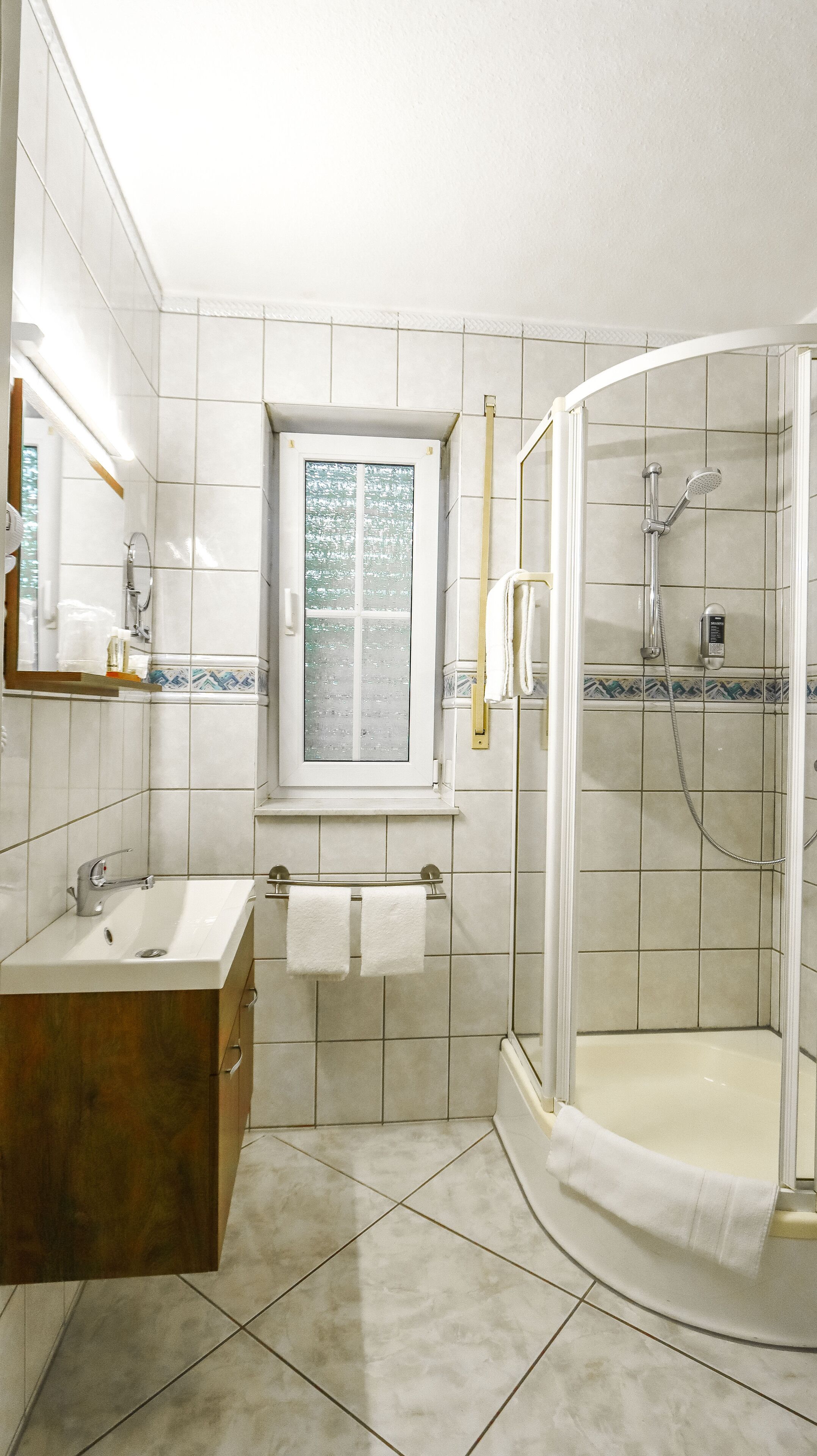 A bathroom with a sink, mirror, window, and a glass-enclosed shower area.