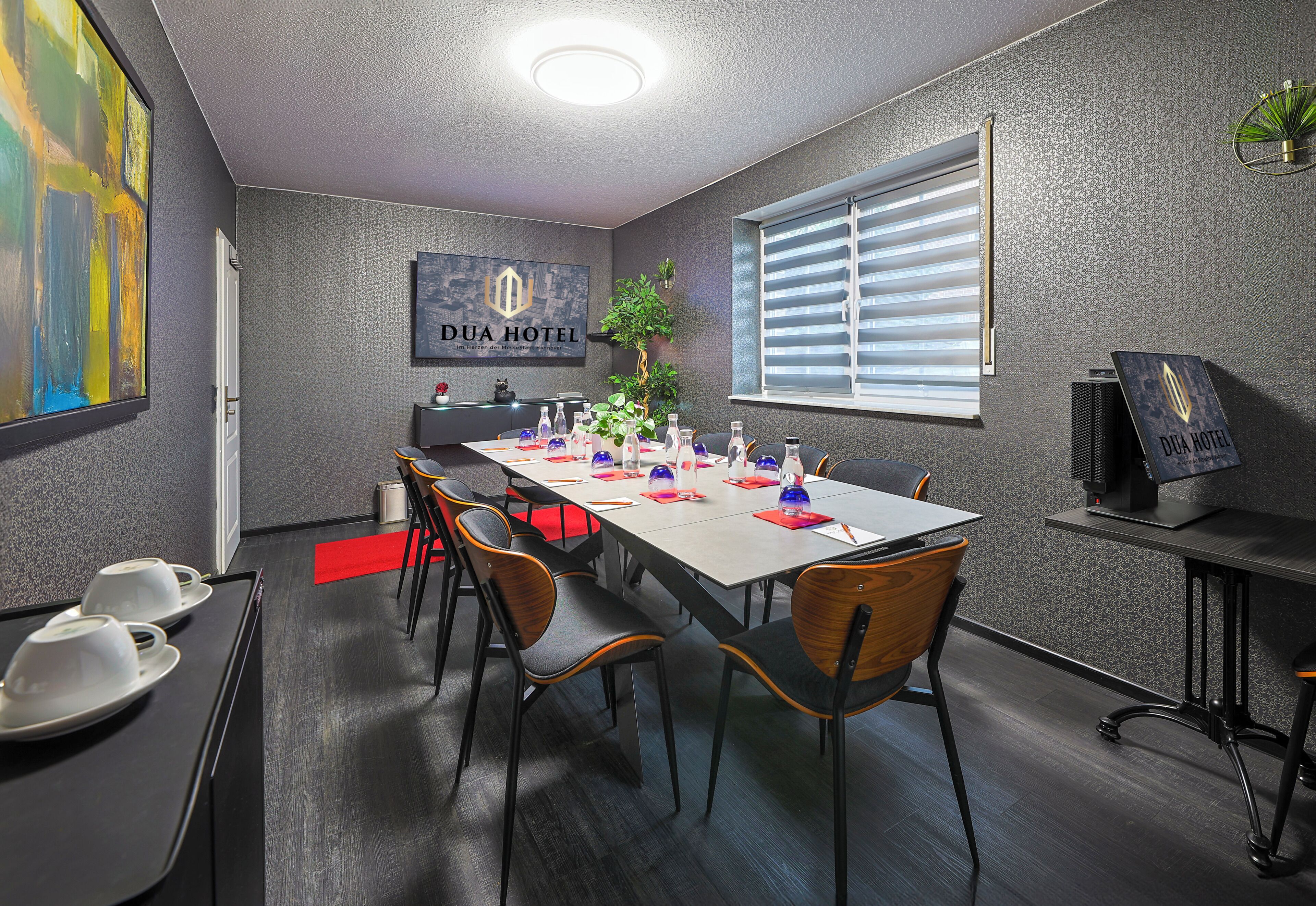 A conference room with a long table, chairs, a plant, and a window with blinds.
