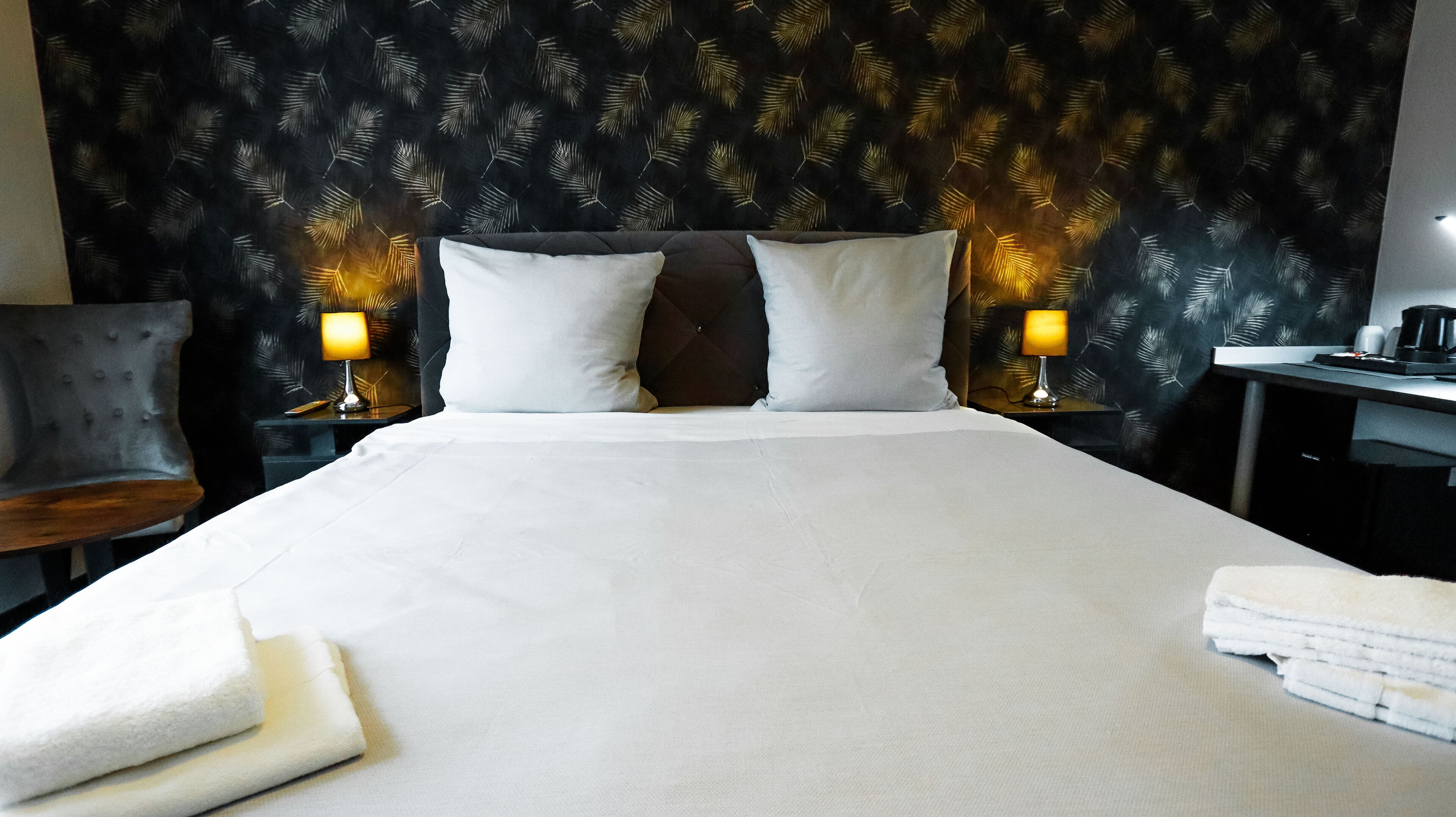 A hotel room with a large bed, two bedside lamps, a desk, and a chair.