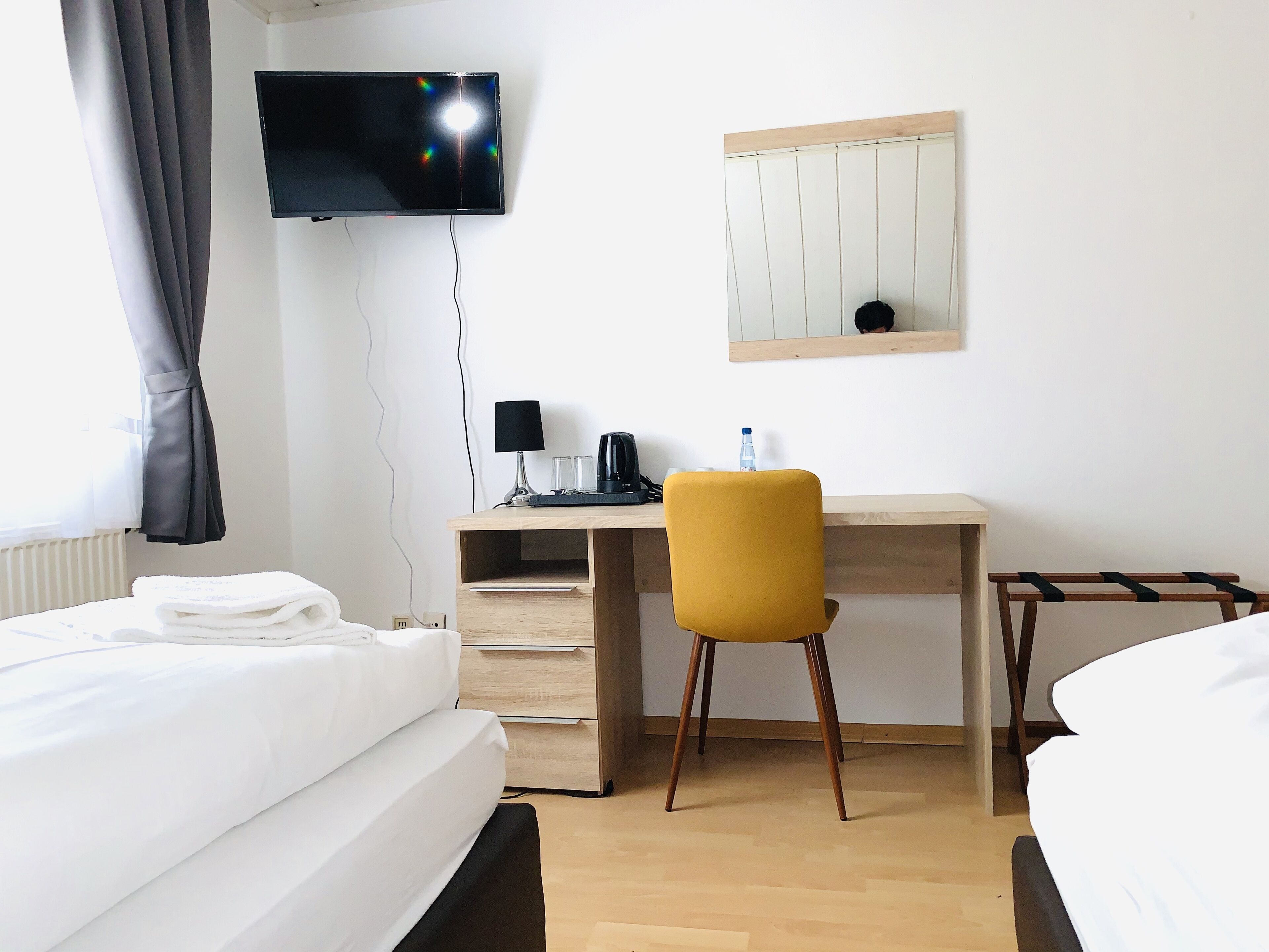 A hotel room with a bed, a desk, a chair, a TV, and a mirror.