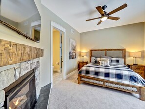 A bedroom with a bed, a fireplace, a ceiling fan, and a door leading to a bathroom. - Golfers dream w/ 5-star experience! Boyne Mountain ski in/out
Garage, fire-pit! (Boyne Falls)