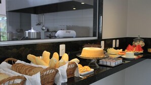 A buffet counter with various breads, a cake, and fruit. - Hotel do Farol (Cubatao)
