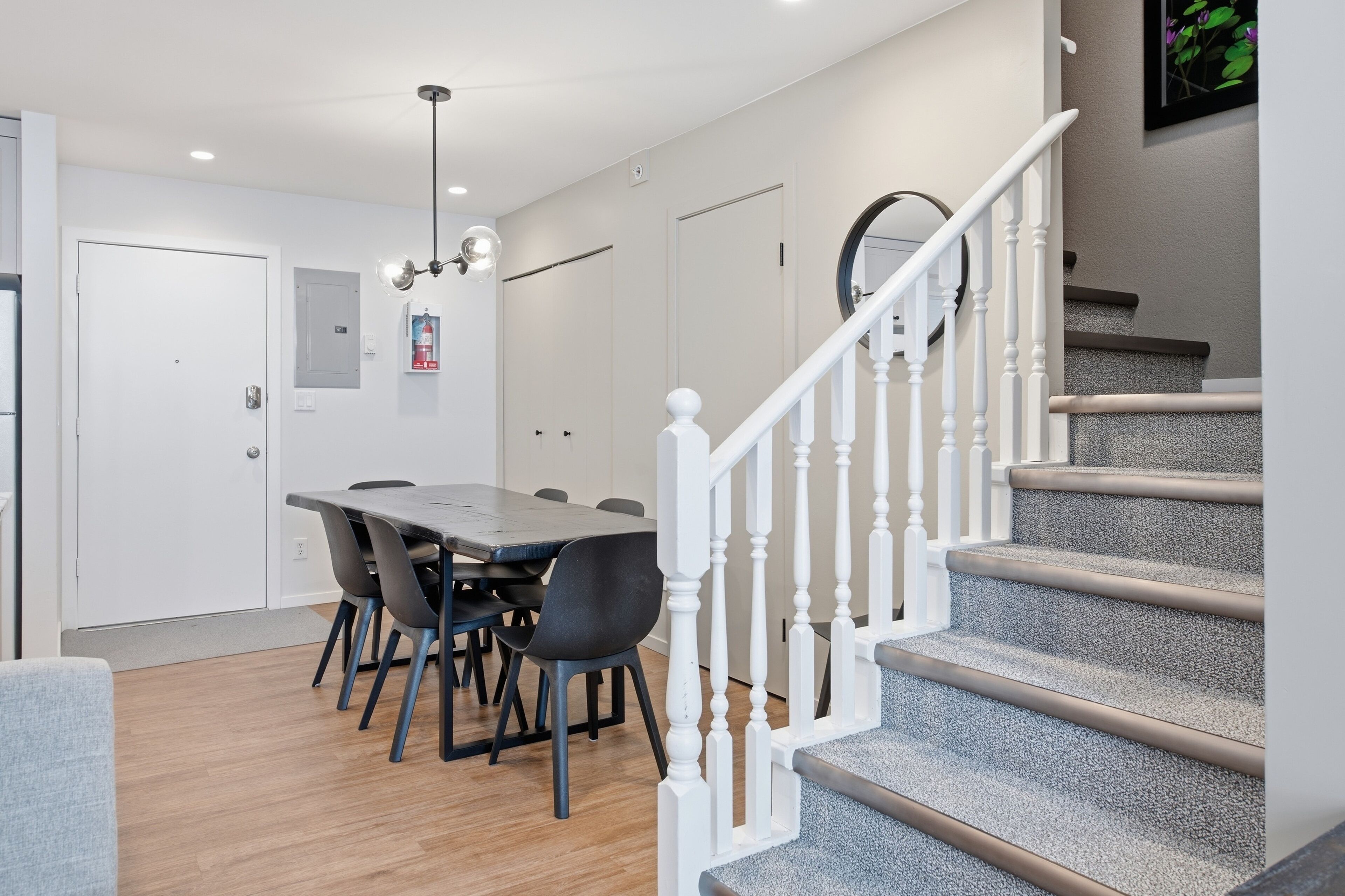 A modern kitchen with a dining area, white staircase, and a ceiling fan.