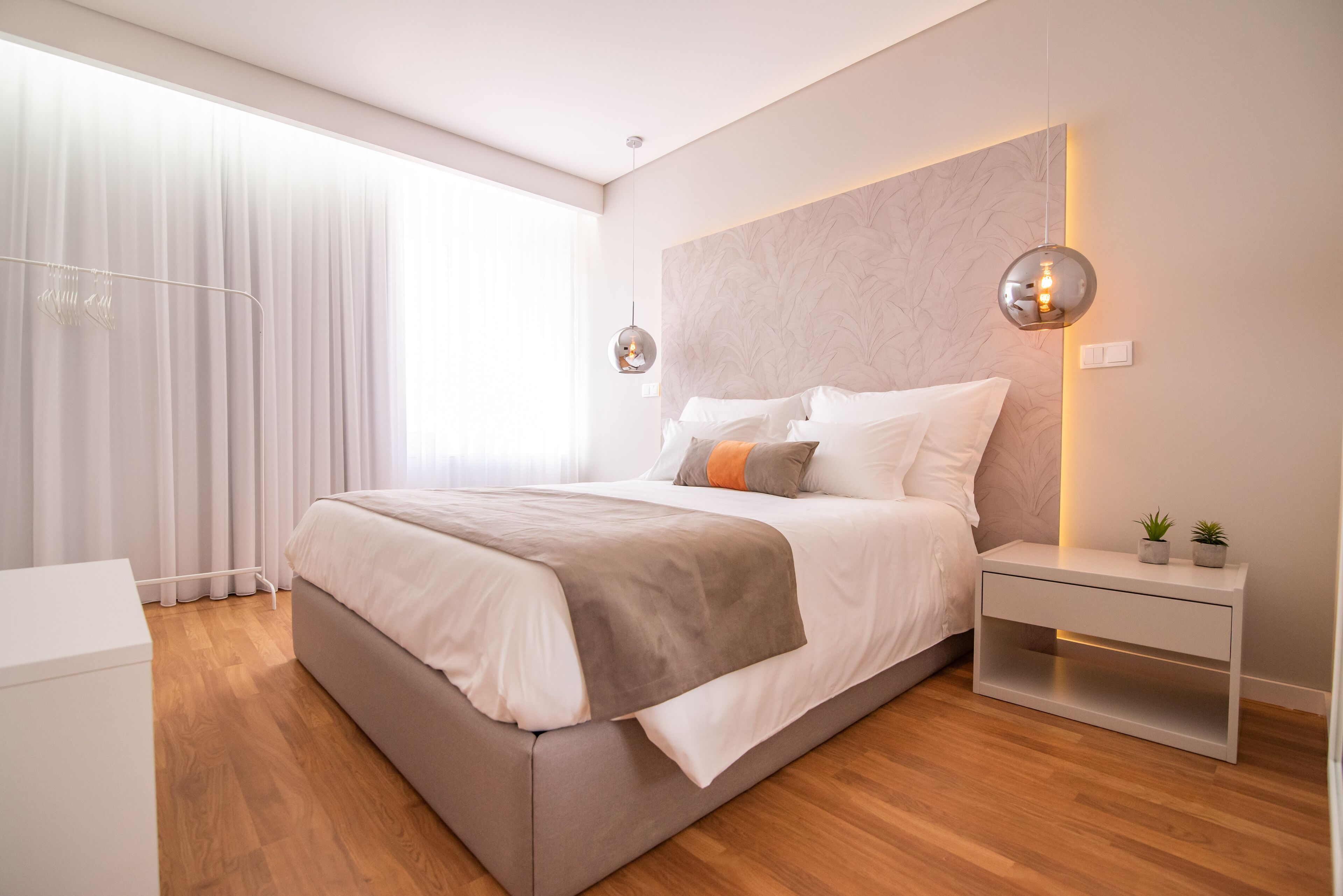 Un dormitorio moderno con una cama grande, mesitas de noche y un ventanal con cortinas.