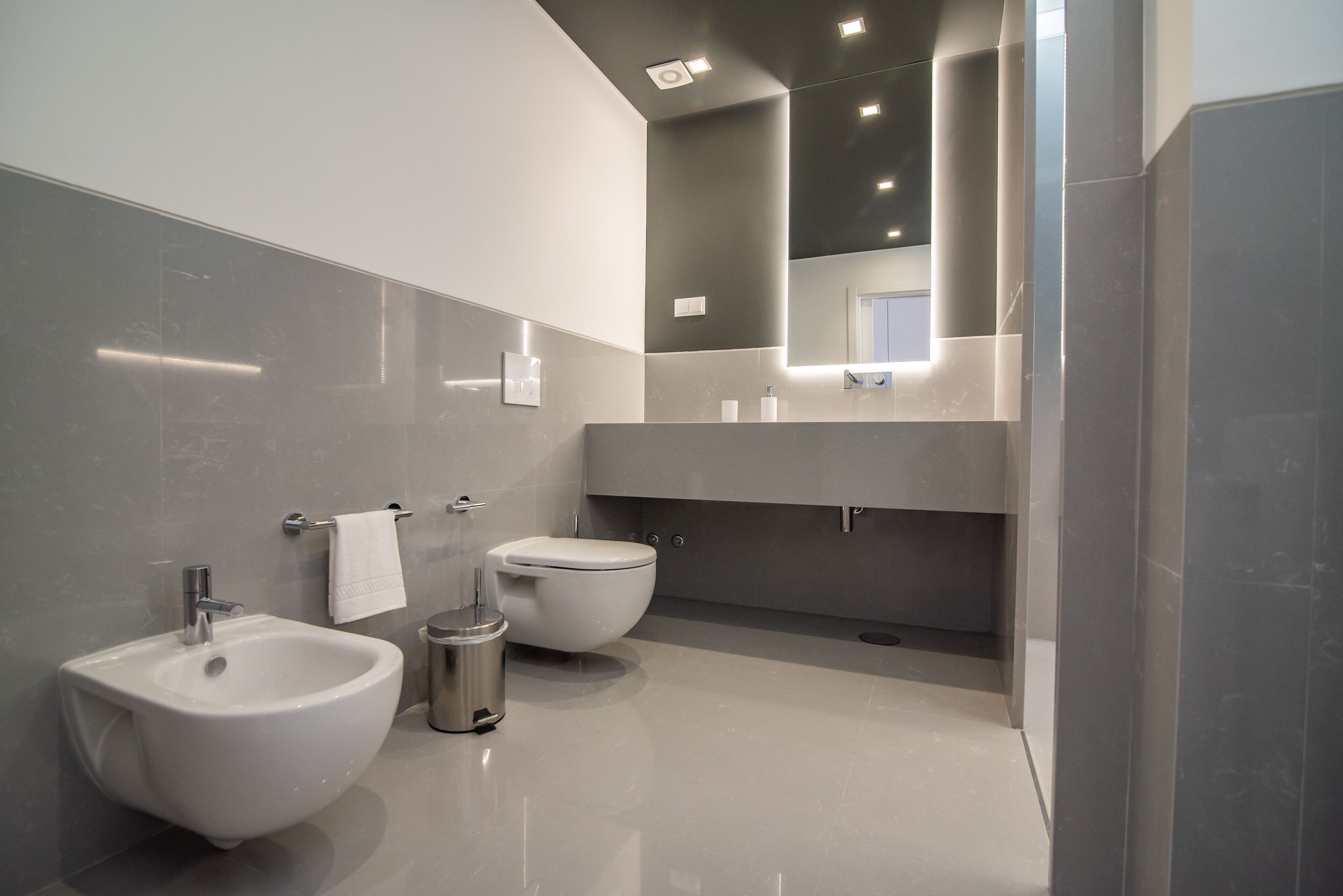 Un baño moderno con bidé, inodoro y un espejo grande.