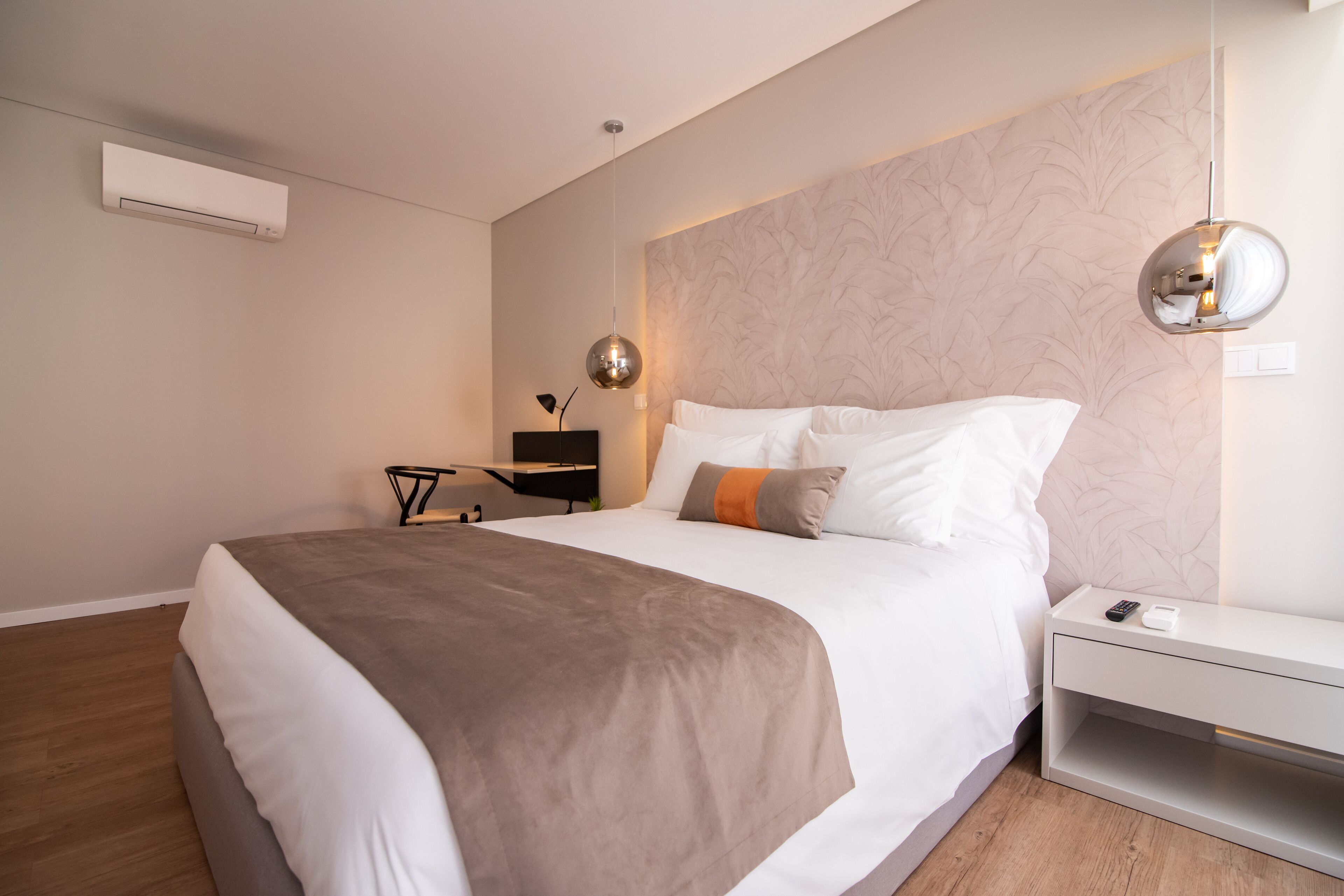 A modern bedroom with a large bed, a bedside table, a wall-mounted air conditioner, and a pendant light.