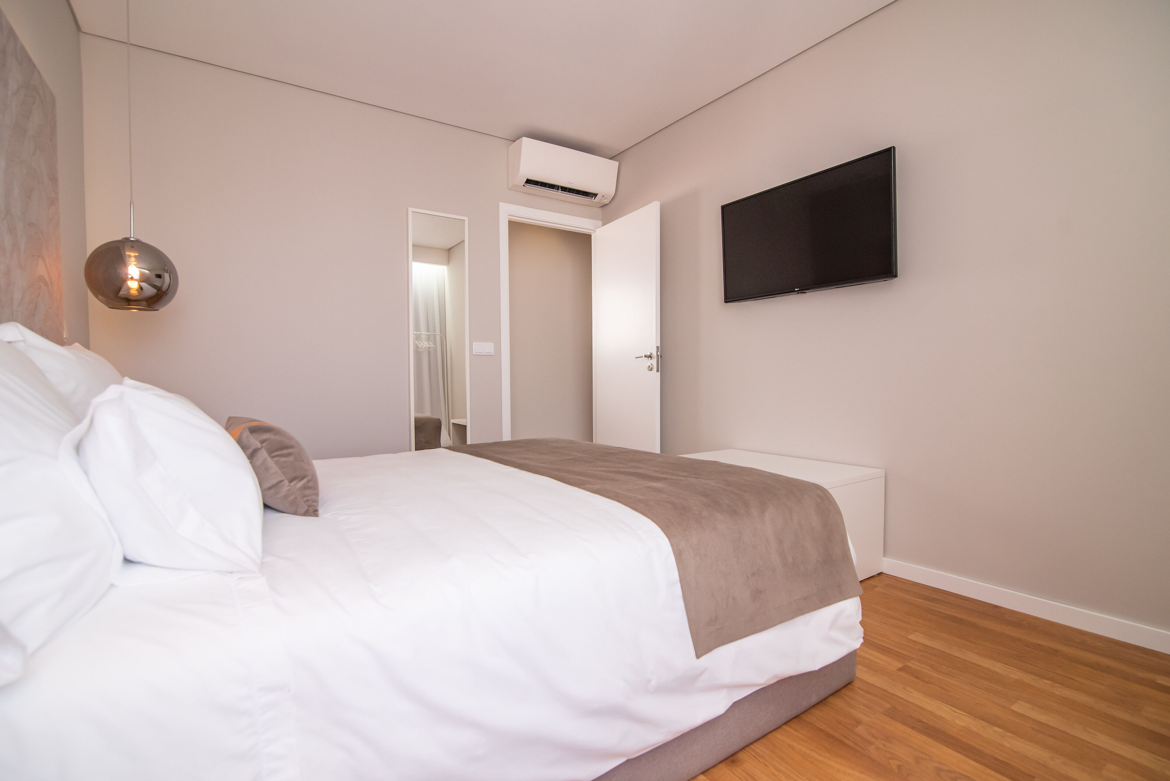 Un dormitorio moderno con cama, televisor montado y equipo de aire acondicionado.