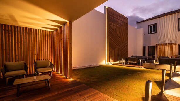 An outdoor patio area with wooden flooring, seating arrangements, and a well-lit ambiance. - Villa Esmeralda (Ponta Delgada)