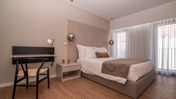 A modern bedroom with a bed, bedside table, chair, desk, and large windows.