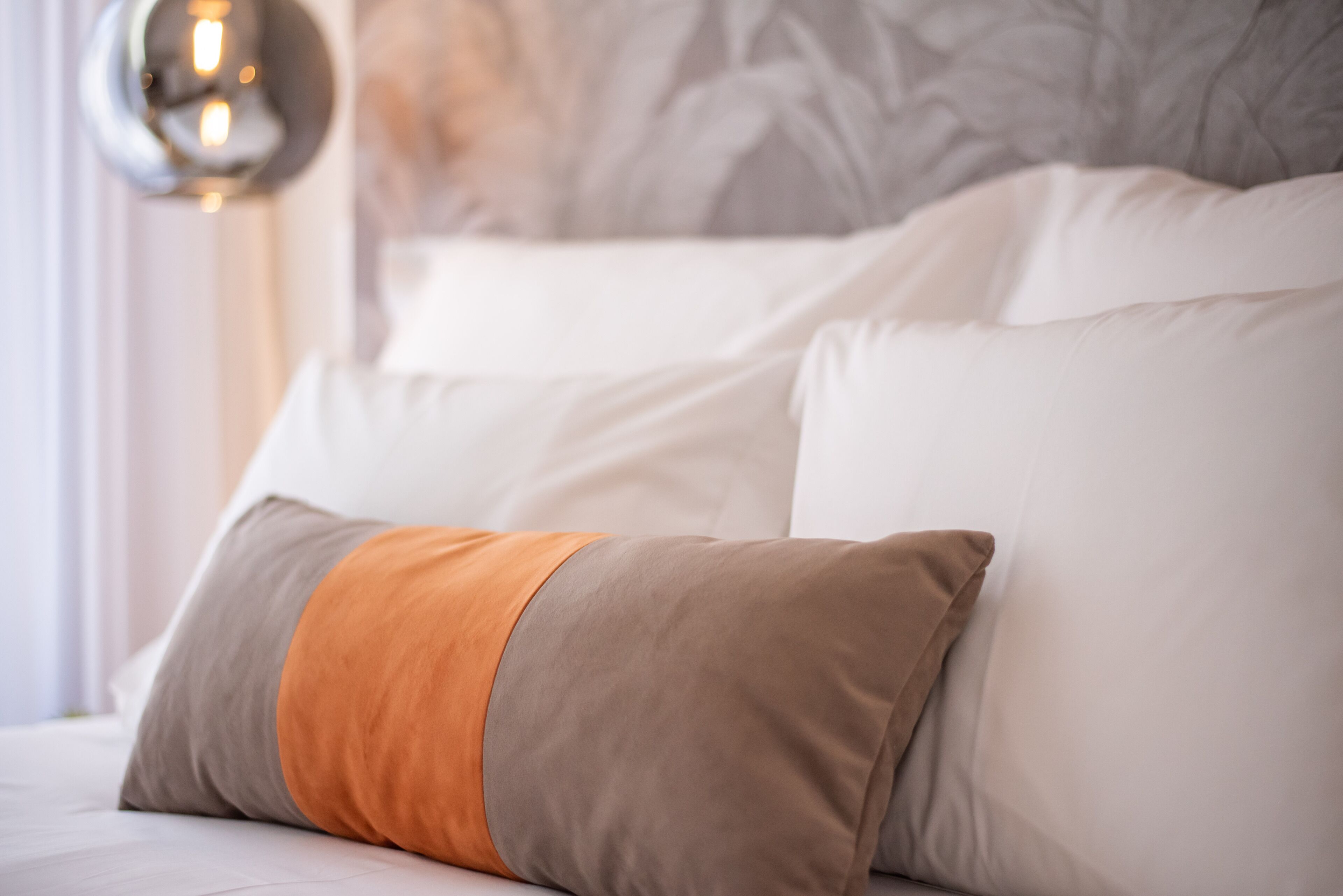 A bed with white and brown pillows, a grey headboard, and a wall-mounted light fixture.