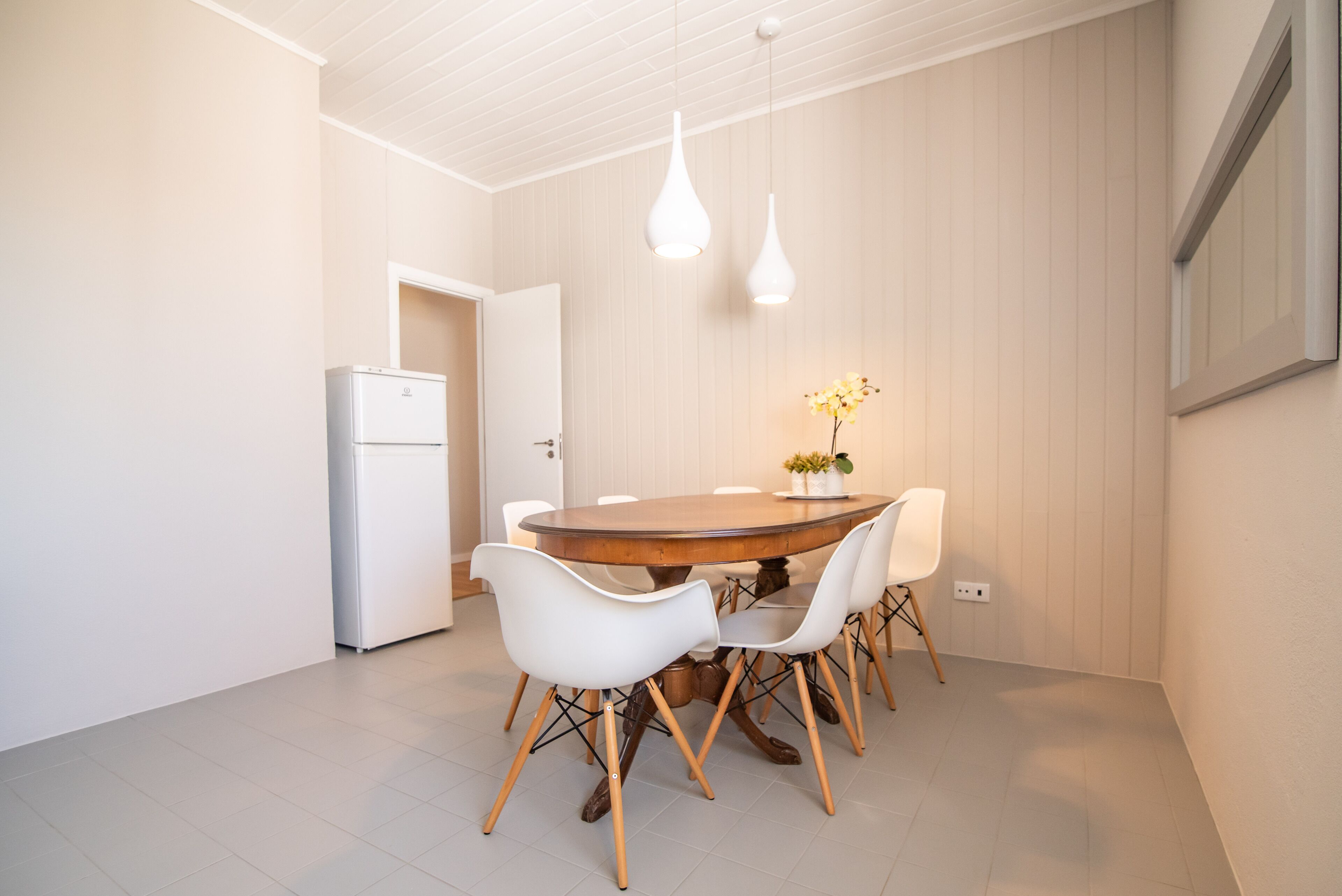 A dining area with a round wooden table, white chairs, and pendant lights.