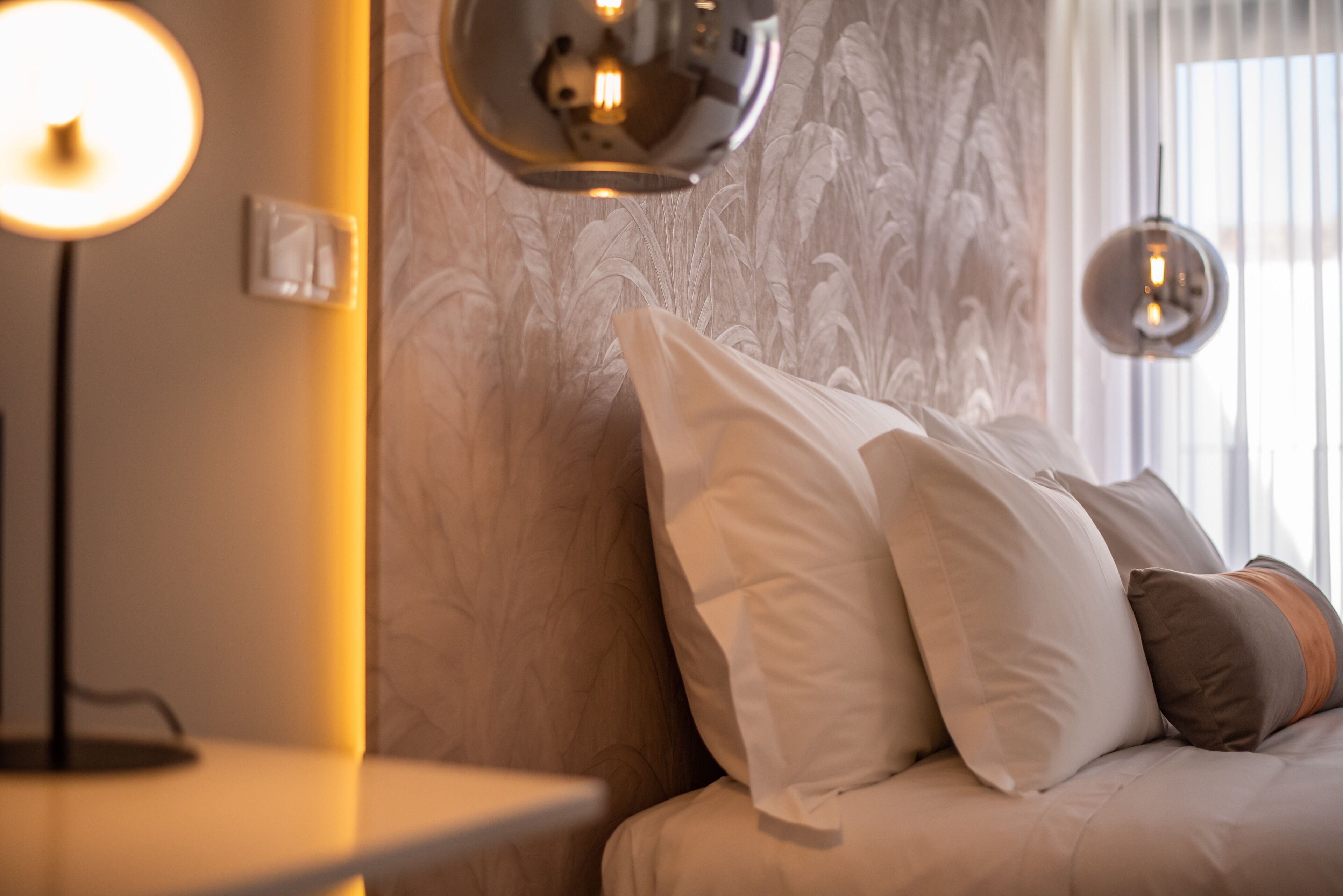 A bedroom with a bed, pillows, a bedside table, and a lamp.