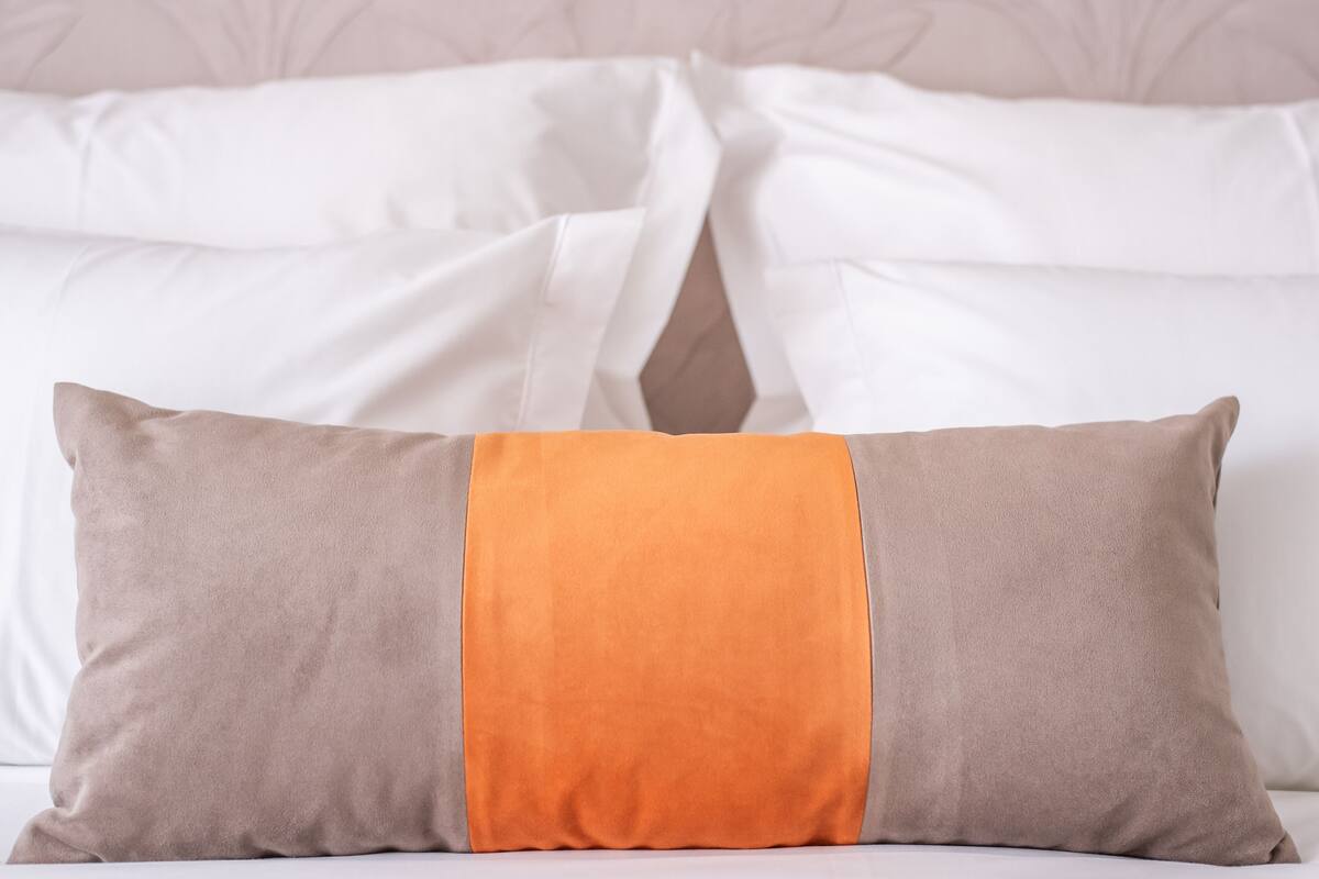 Una cama individual con ropa blanca de cama y un cojín de diseño marrón y naranja.