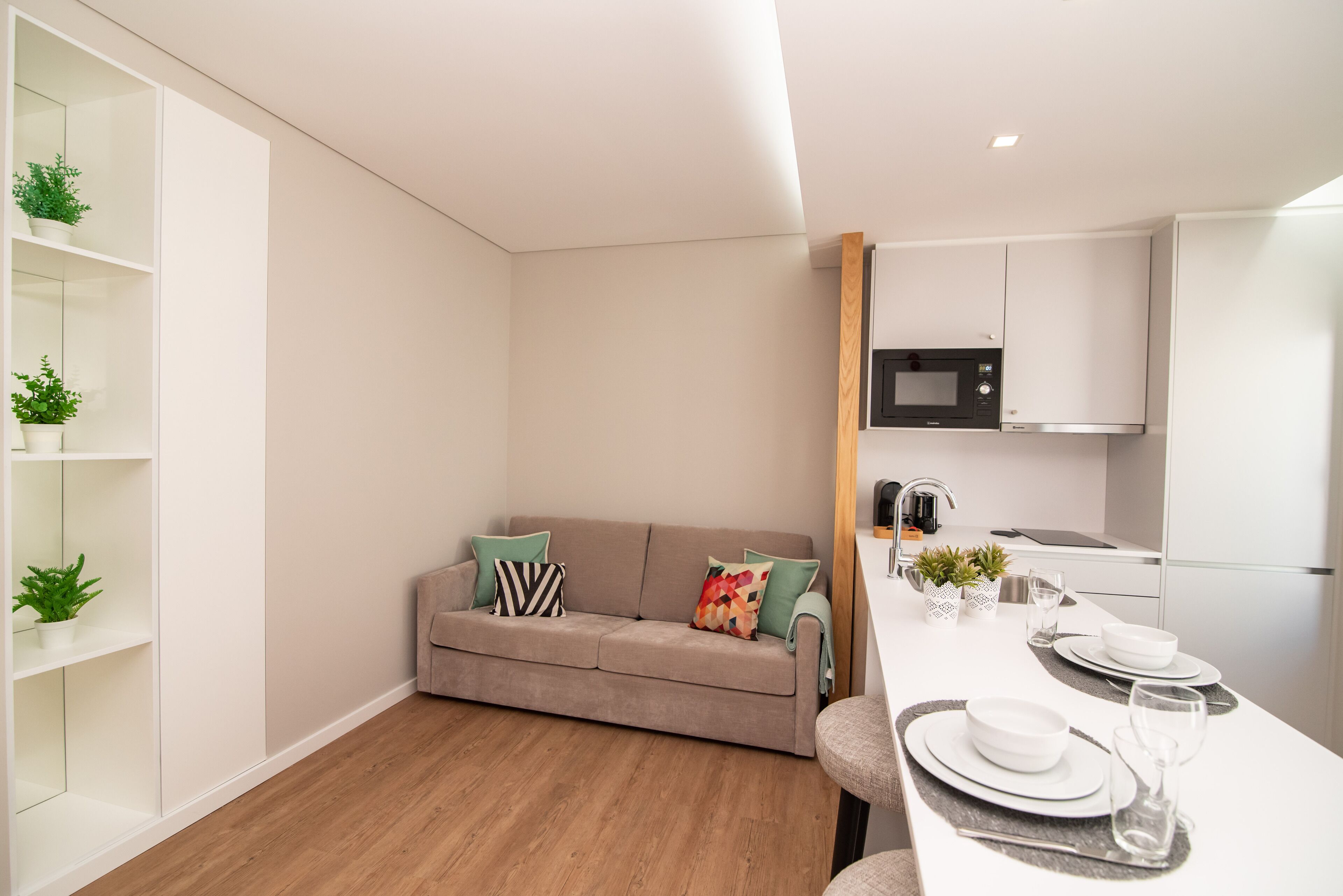 A modern living room with a sofa, a dining table set with plates and glasses, and a kitchen area with a microwave.