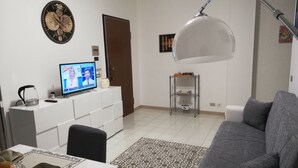 A living room with a grey sofa, a coffee table, a TV on a white cabinet, a patterned rug, and a wall clock. - Madrigio ... at home (Casamassima)