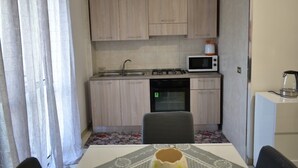A compact kitchen with a sink, stove, microwave, and oven. There is a dining table with a chair in front. - Madrigio ... at home (Casamassima)