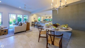 A modern kitchen with a dining area, featuring a round table set for four, a sofa, and a large window with a view of greenery. - **MIDTOWN MOSAIC @ MIDTOWN** Home & Pool + Last Key White Glove Service... (Key West)