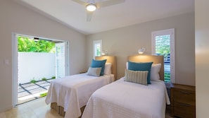 A hotel room with two beds, a ceiling fan, and a view of greenery outside.