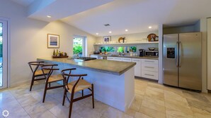 A modern kitchen with a central island, bar stools, a refrigerator, and a view of greenery outside. - **MIDTOWN MOSAIC @ MIDTOWN** Home & Pool + Last Key White Glove Service... (Key West)