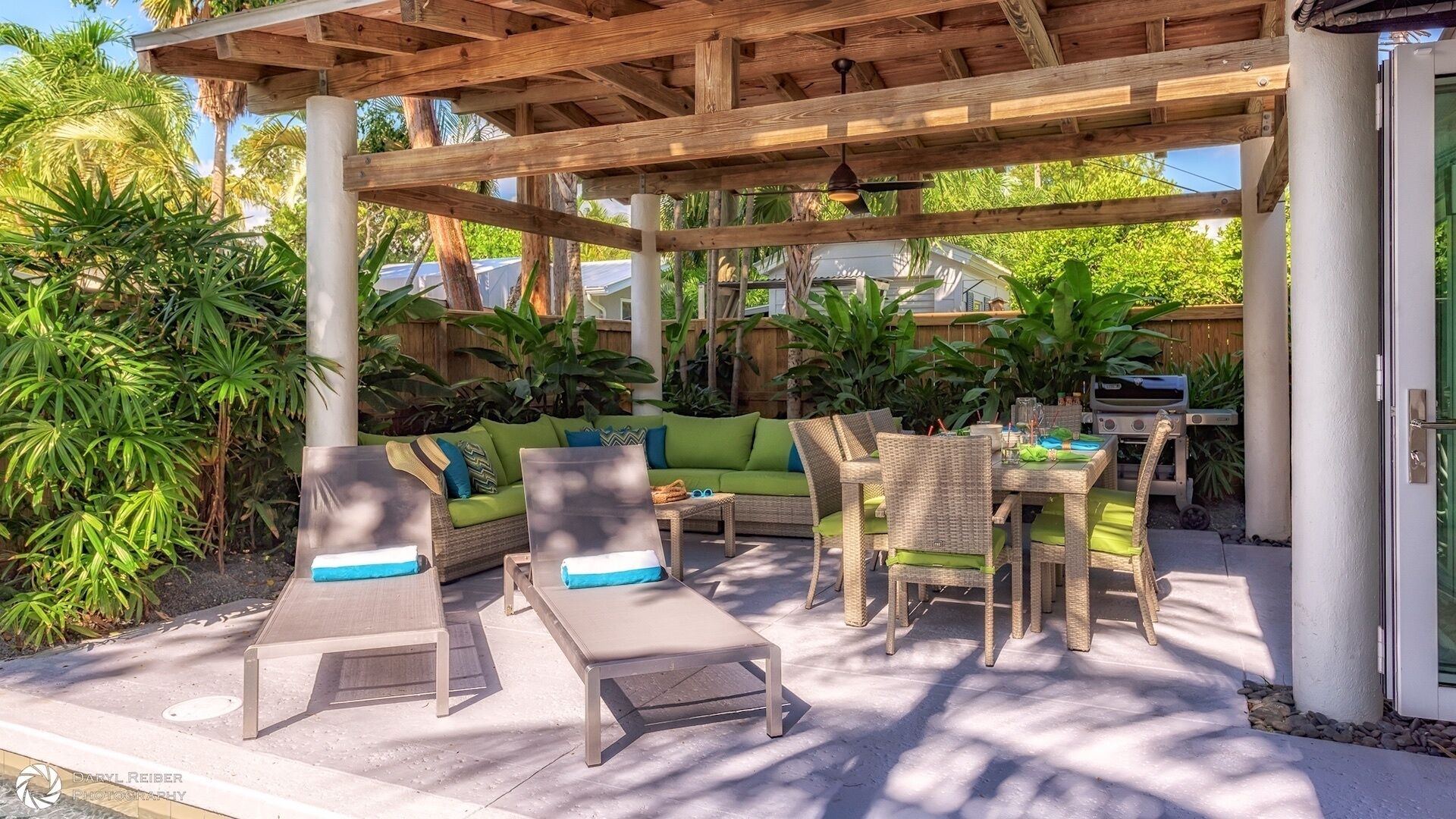 An outdoor patio with a wooden pergola, lounge chairs, a dining table, and a grill.