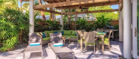 An outdoor patio with a wooden pergola, lounge chairs, a dining table, and a grill.