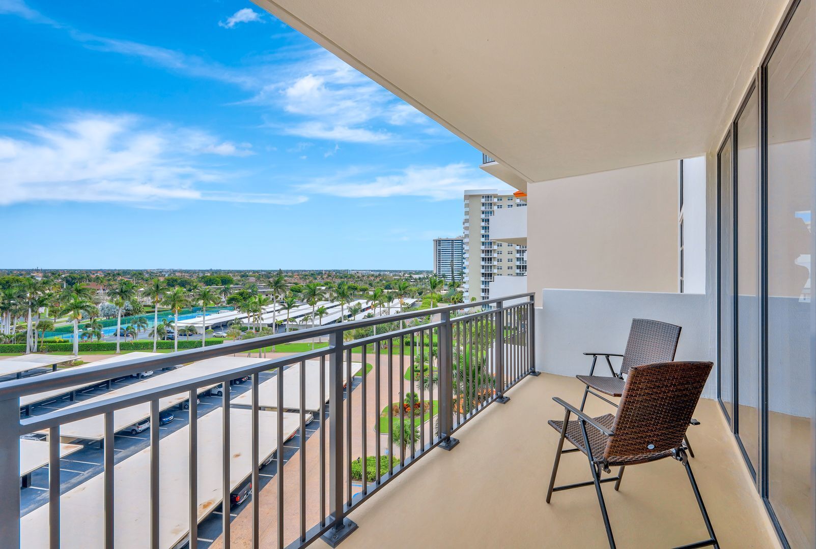 A balcony with a view of a parking lot and buildings, and a chair.