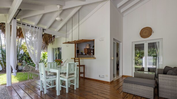 Een ruime woonkamer met een houten vloer, een eettafel met stoelen, een bank en een hangplank met decoratieve objecten.