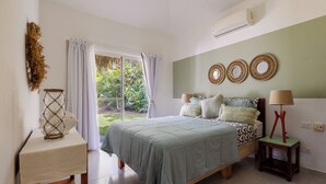 Een slaapkamer met een bed, nachtkastje, lamp en uitzicht op groen.