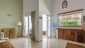 Een ruime woonkamer met een bank, een salontafel en een eettafel. Er is een glazen schuifdeur naar een balkon met uitzicht op groen.
