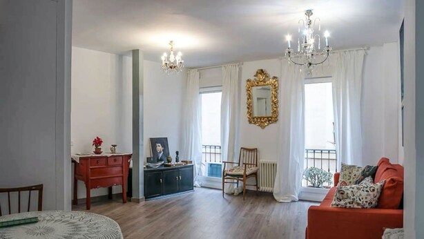A living room with a red sofa, a wooden dining table with chairs, a black cabinet, and a large mirror on the wall. - Apartment, center of Madrid, Embajadores area (Madrid)