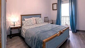 A bedroom with a large bed, a bedside table, a lamp, a chair, and a window with curtains. - Apartment, center of Madrid, Embajadores area (Madrid)