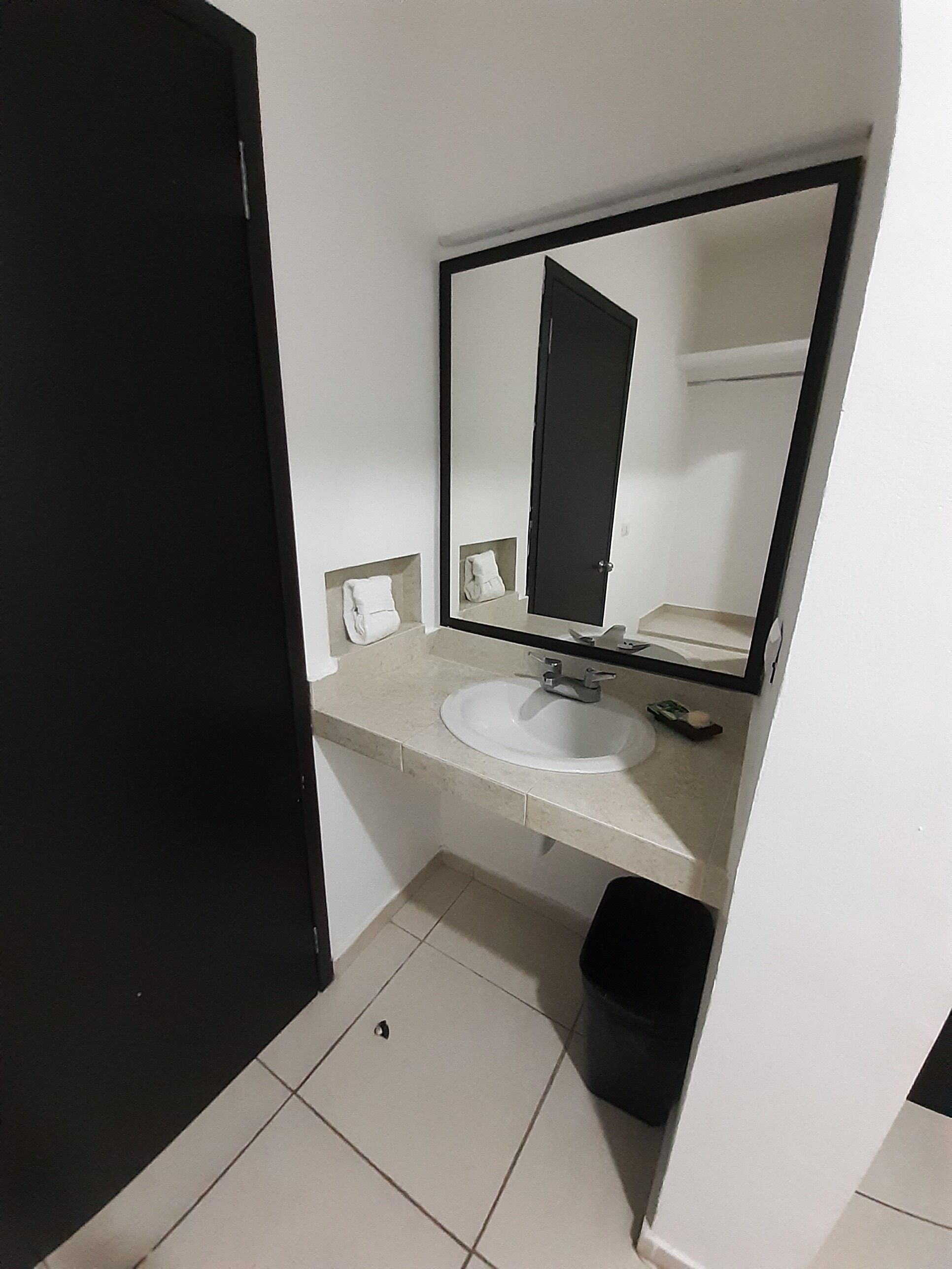 A small bathroom with a white sink, a mirror, and a black trash bin.