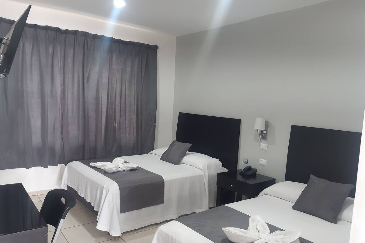 A hotel room with two beds, a desk, a chair, and a nightstand with a phone.