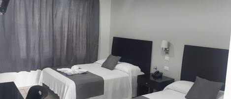 Quarto de hotel com duas camas, uma escrivaninha, uma cadeira e uma mesinha de cabeceira com telefone.