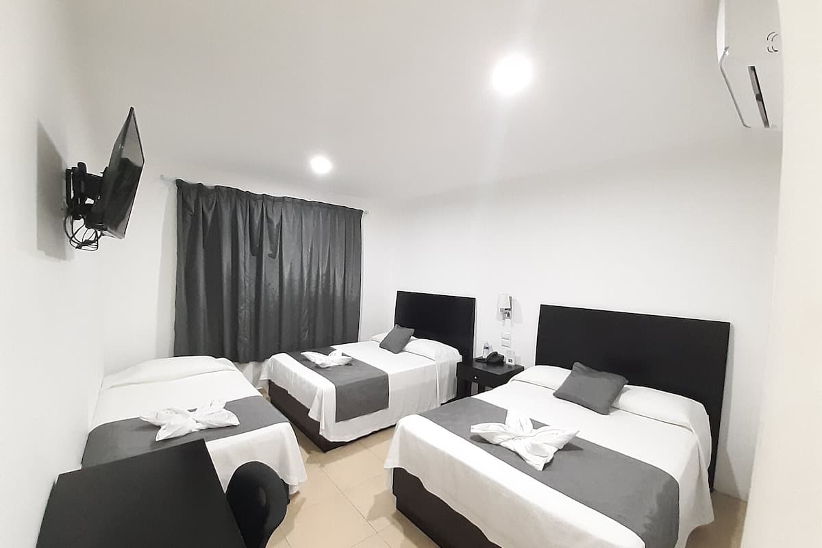 A hotel room with two beds, a TV mounted on the wall, a small table, and a curtain.