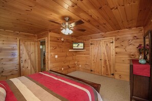 A wooden cabin bedroom with a bed, a ceiling fan, a mounted TV, and a wooden wardrobe.