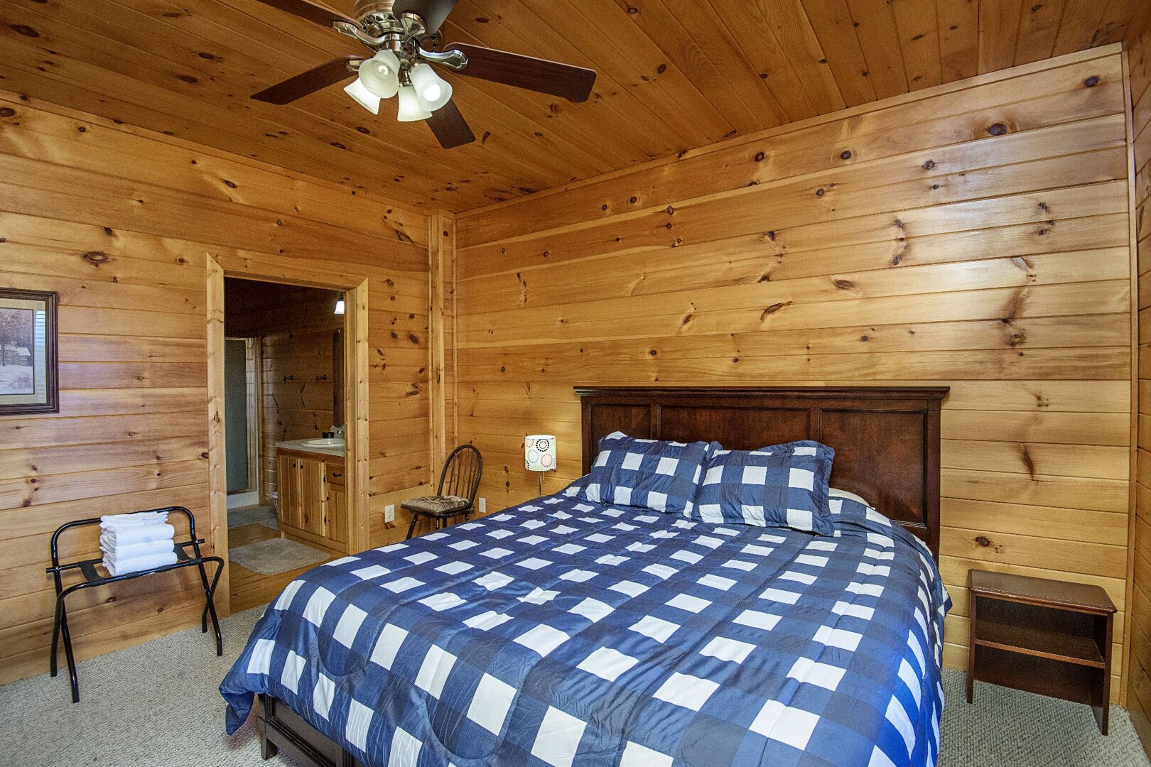 Une chambre dans une cabane en bois, avec un lit, un ventilateur de plafond et une petite table de chevet en bois.