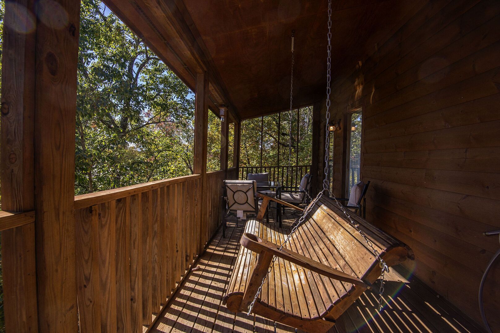 A wooden deck with a swing chair and a table, overlooking a forested area.