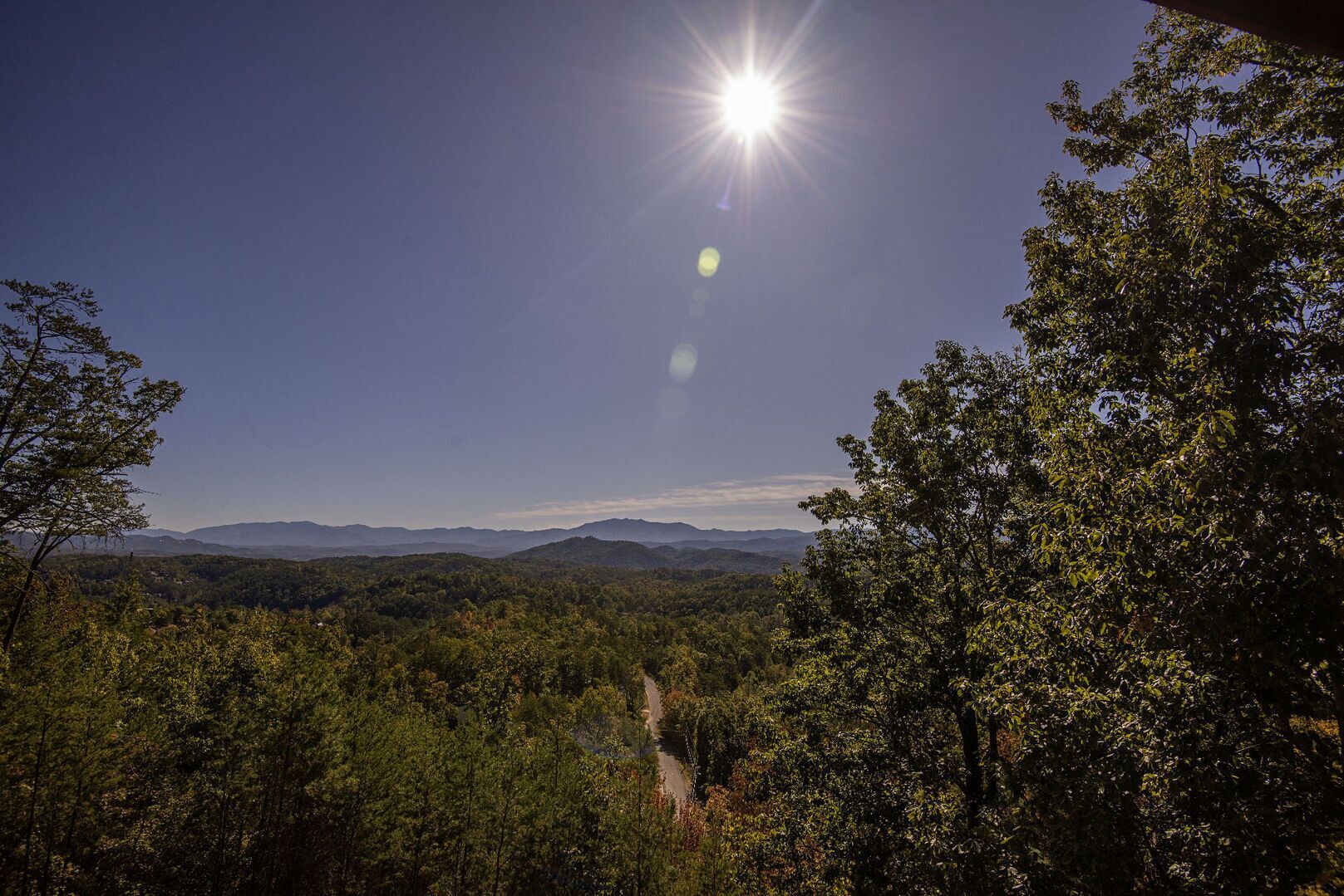 A mountainous landscape with a clear sky and a sun shining through the trees.