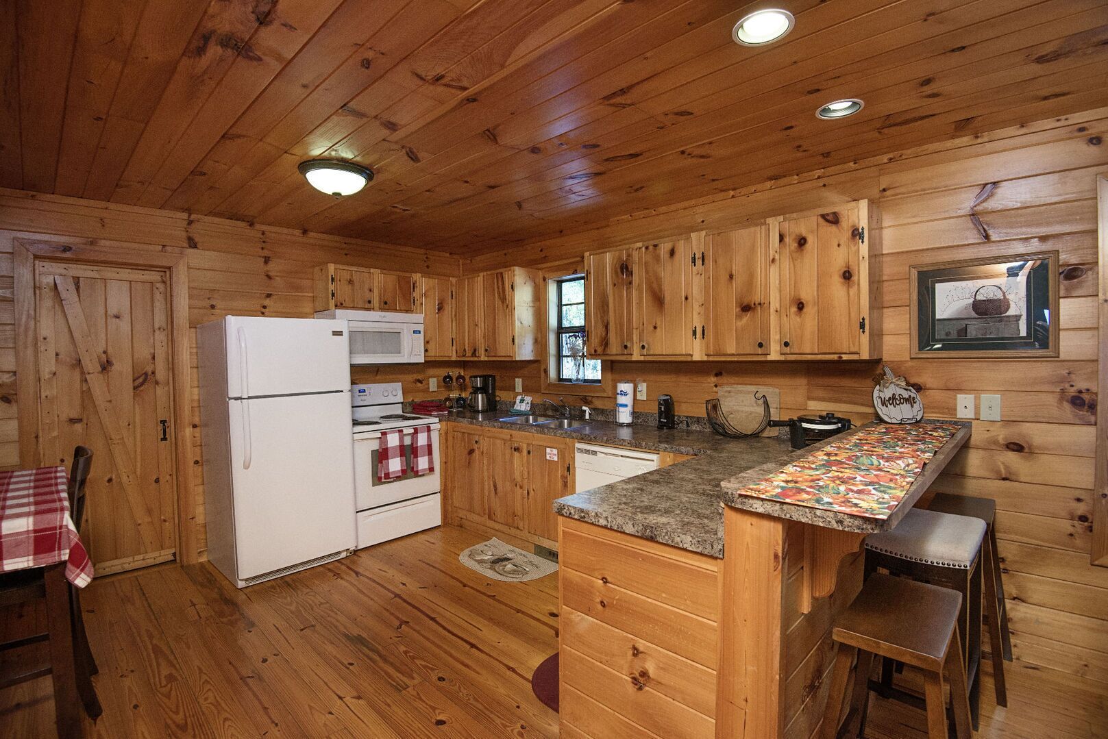A wooden cabin-style kitchen with a refrigerator, stove, microwave, and wooden cabinets.