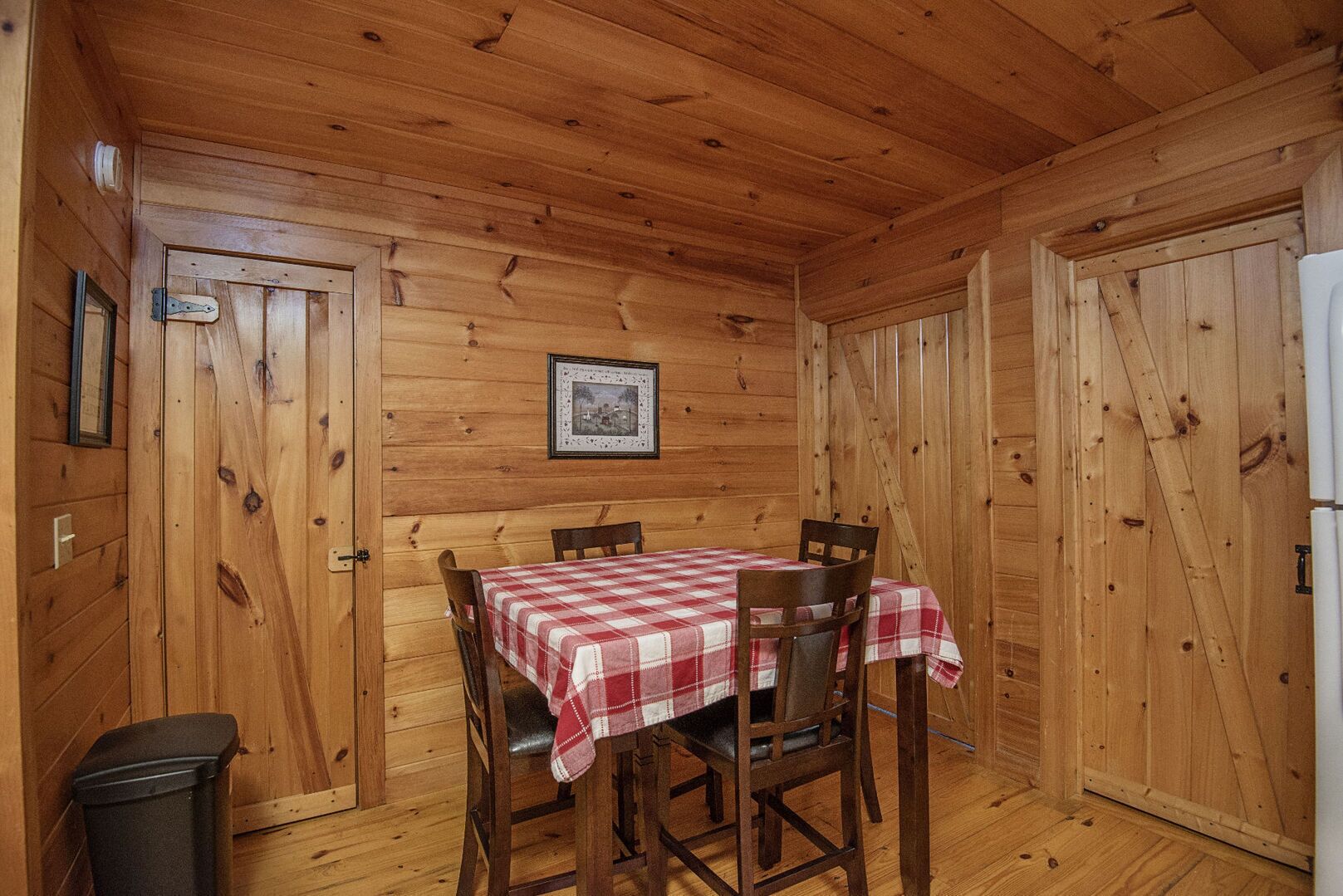 Um quarto com painéis de madeira, uma mesa posta para dois, um quadro na parede e uma lixeira.