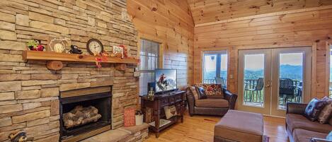 A cozy cabin interior with a stone fireplace, wooden walls, and a balcony with a scenic view.