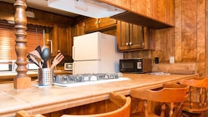 Una cocina con armarios de madera, un refrigerador blanco, un microondas y una barra de madera con sillas.