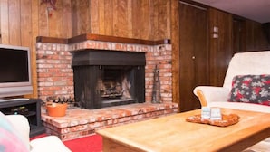 Una sala de estar con chimenea de ladrillo, televisor de pantalla plana y una mesa de centro de madera.