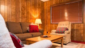 Una sala de estar acogedora con un revestimiento de madera, un sofá, un sillón, una mesa de centro y una lámpara.