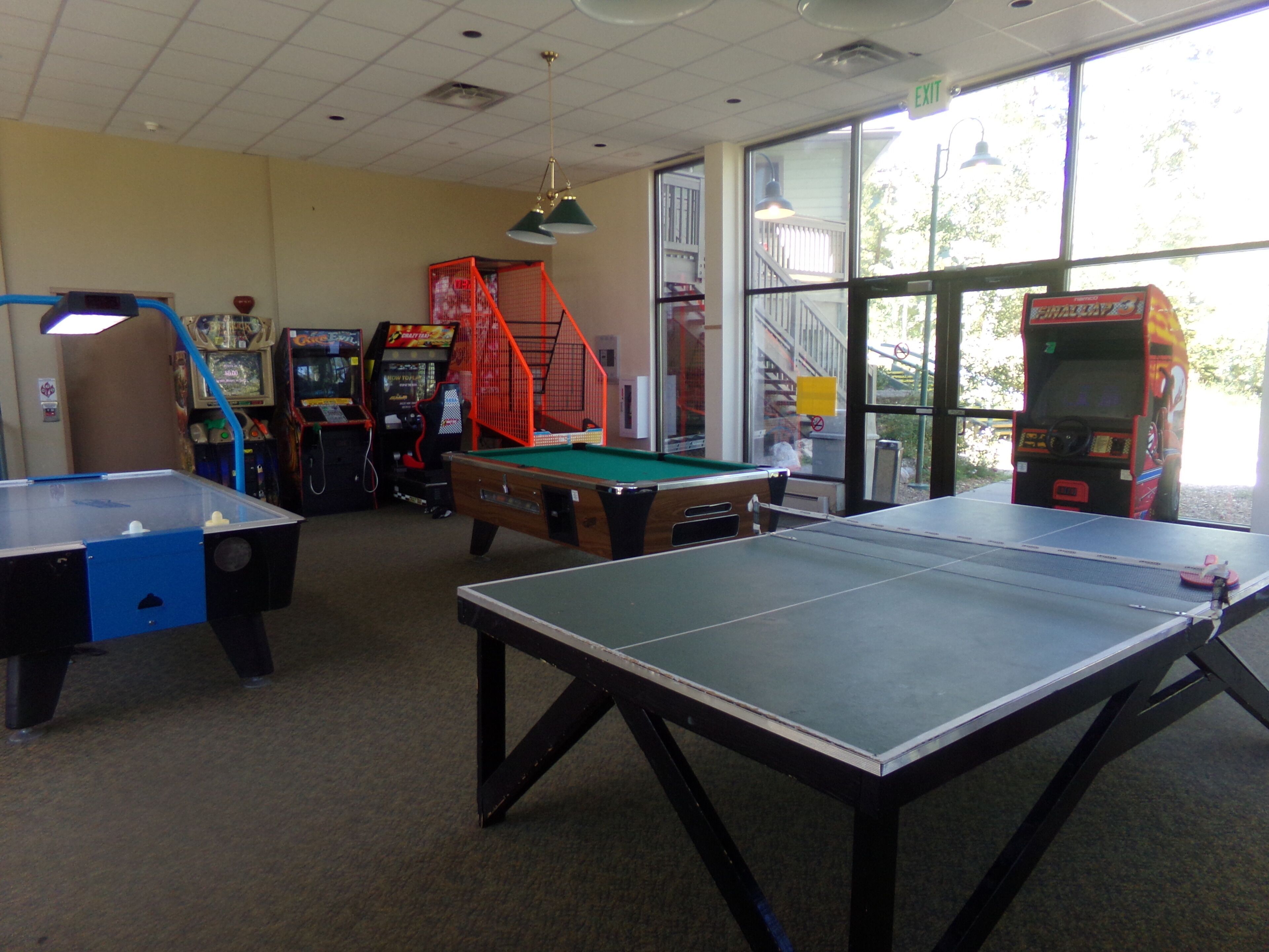 Una habitación con mesa de billar, mesa de ping pong y juegos de arcade.