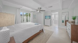 Un dormitorio moderno con una cama grande, ventilador de techo, televisor y vistas al exterior.