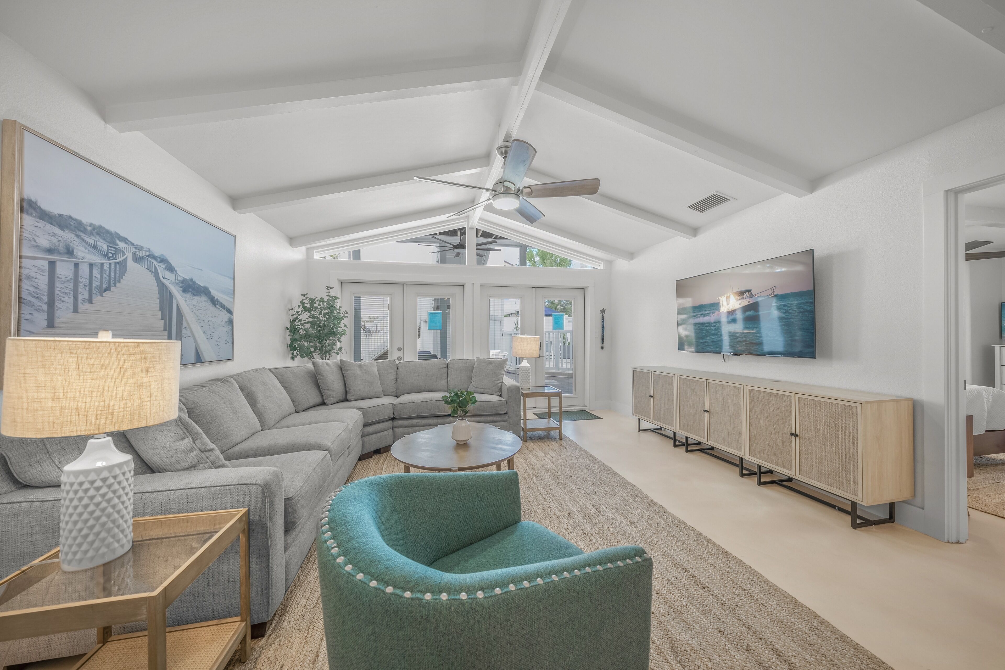 A spacious living room with a large sectional sofa, a teal armchair, a round coffee table, and a television mounted on the wall.