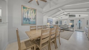 Un comedor amplio con una mesa y sillas de madera, un ventilador de techo y un cuadro de veleros en la pared.