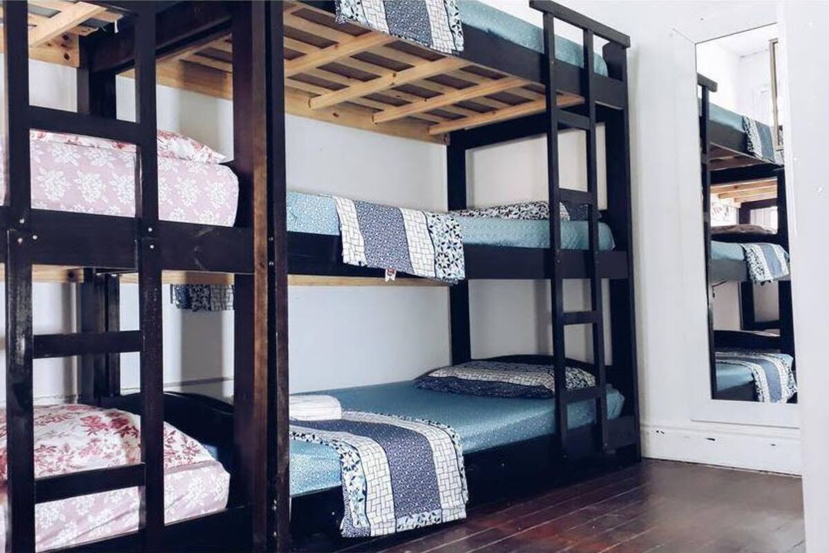 Une chambre avec un lit superposé, des structures en bois, une literie à motifs et un plancher en bois.